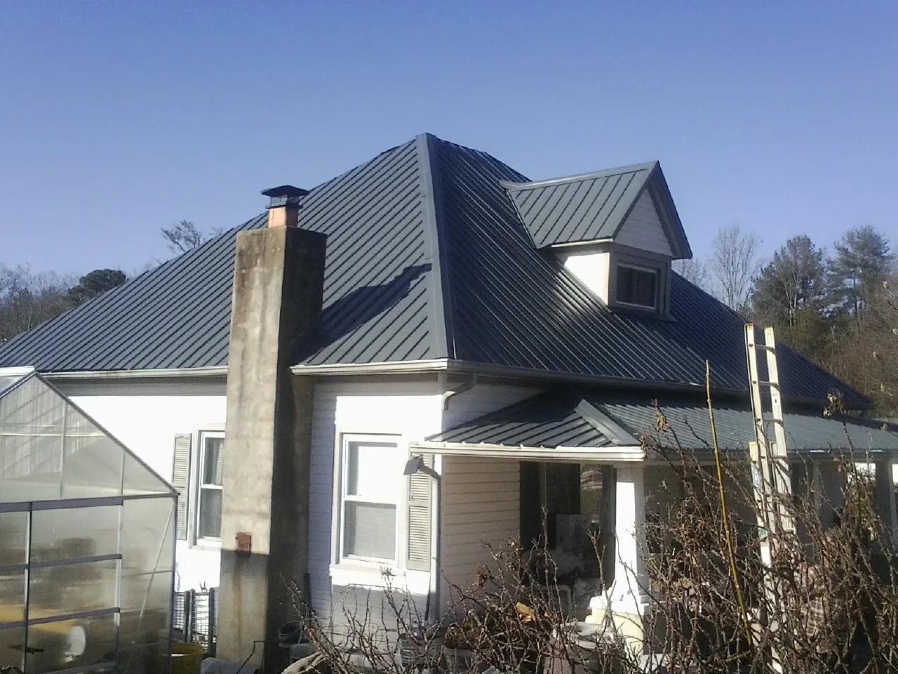 Dark blue standing seam metal roof on a white farmhouse with dormer — Slate & Tile Roof Repair by Roofing Brothers in Mc Clelland