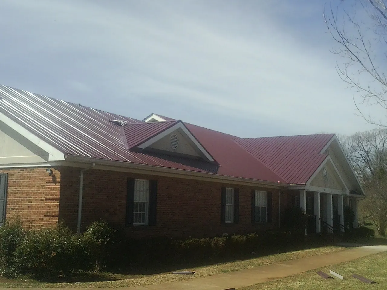 Red metal roof with gabled entries on a long brick building, from a Hail Damage Roof Repair job in Mc Clelland