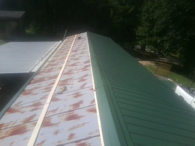 Old rusted panels beside newly installed green metal roofing — Wind Damage Roof Repair by Roofing Brothers in Mc Clelland