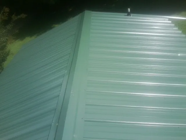 New green metal panels meeting at the ridge of a roof — Flat Roof Repair work by our crew in Mc Clelland