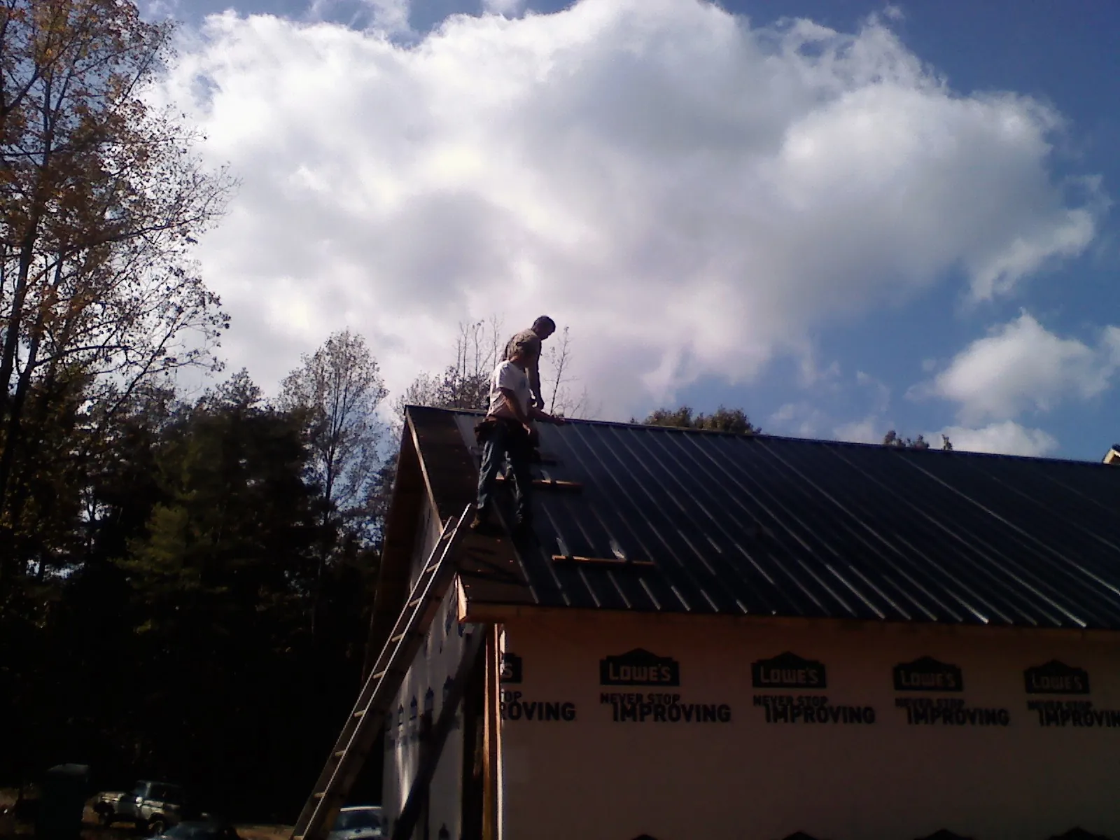 Roofer fastening dark metal panels high against a cloudy sky, from a Roof Inspection job in Mc Clelland