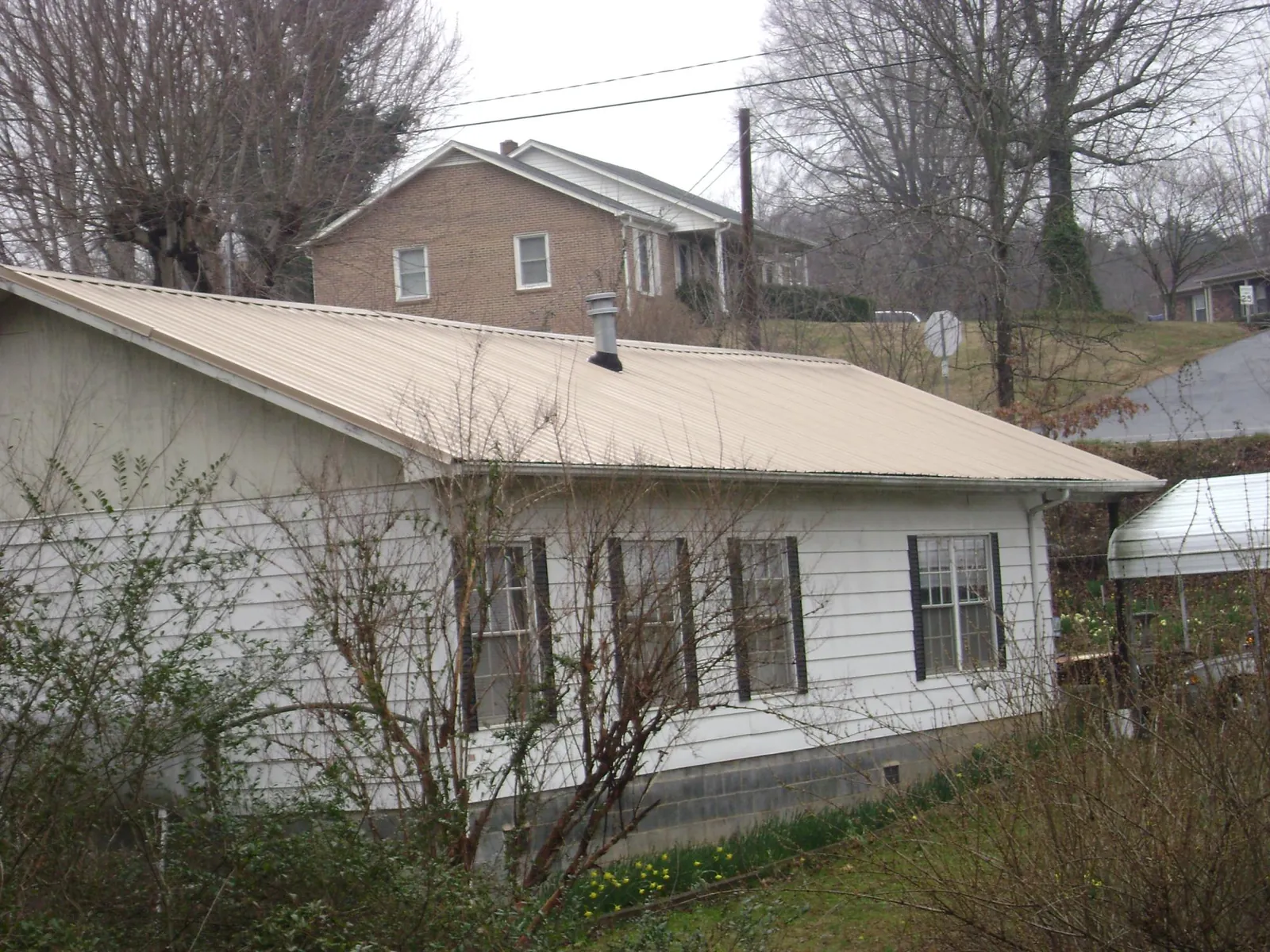 Tan metal roof on a white sided house set into a hillside — Commercial Roofing by Roofing Brothers in Mc Clelland